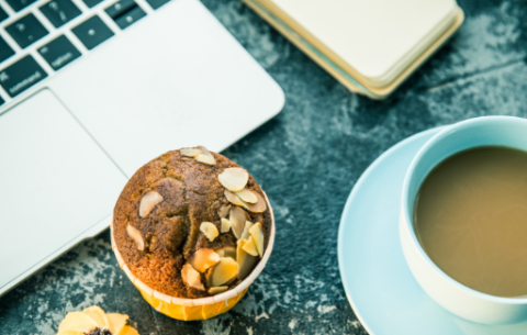 desk with coffee mug, cakes and a laptop keyboard
